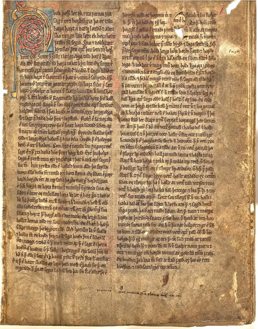 Photograph of a stained, hole-worn vellum manuscript page in two columns of dense brown medieval script, with a large red-and-blue decorated initial letter at the top left.